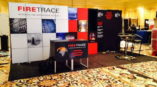 Trade show backdrop for FireTrace featuring bold red and black graphics with product information and a display counter.