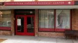 Monument sign for Mahakaruna Kadampa Buddhist Center with red awning and window graphics displaying a Buddha image.