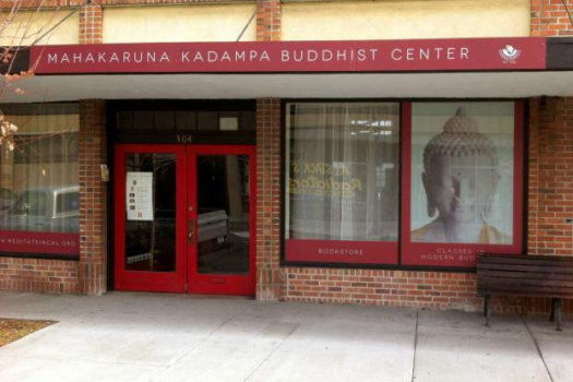Monument sign for Mahakaruna Kadampa Buddhist Center with red awning and window graphics displaying a Buddha image.