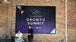 A graphic hanging on a wall advertising the eCommerce Growth Summit.