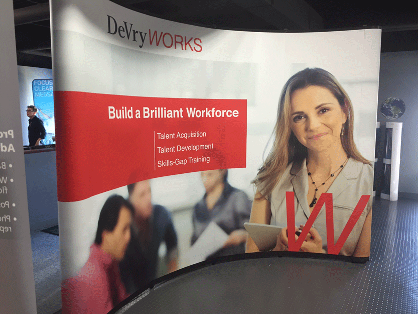 Curved trade show backdrop for DeVryWORKS featuring the tagline 'Build a Brilliant Workforce' alongside service details.