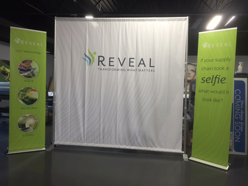 Trade show backdrop displaying the REVEAL brand logo and tagline, flanked by retractable banners with methodology details.