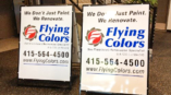 A-frame signs for Flying Colors renovation services featuring contact information and branding in a lobby setting.