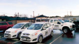 Fleet wrap vehicles for Automated Gate Systems parked in a lot, showcasing white cars with blue and orange graphics.