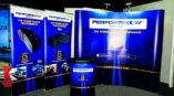 Trade show backdrop for Performaxx featuring brake pad graphics with blue and yellow color scheme and promotional text.