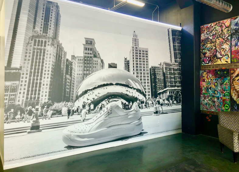 Black and white wall mural featuring a large shoe in front of the Chicago Cloud Gate sculpture.