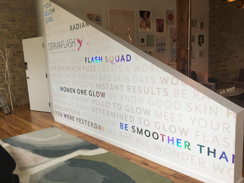 Environmental wall graphics for Dermaflash, featuring inspirational phrases and branded logo on white wall surface.