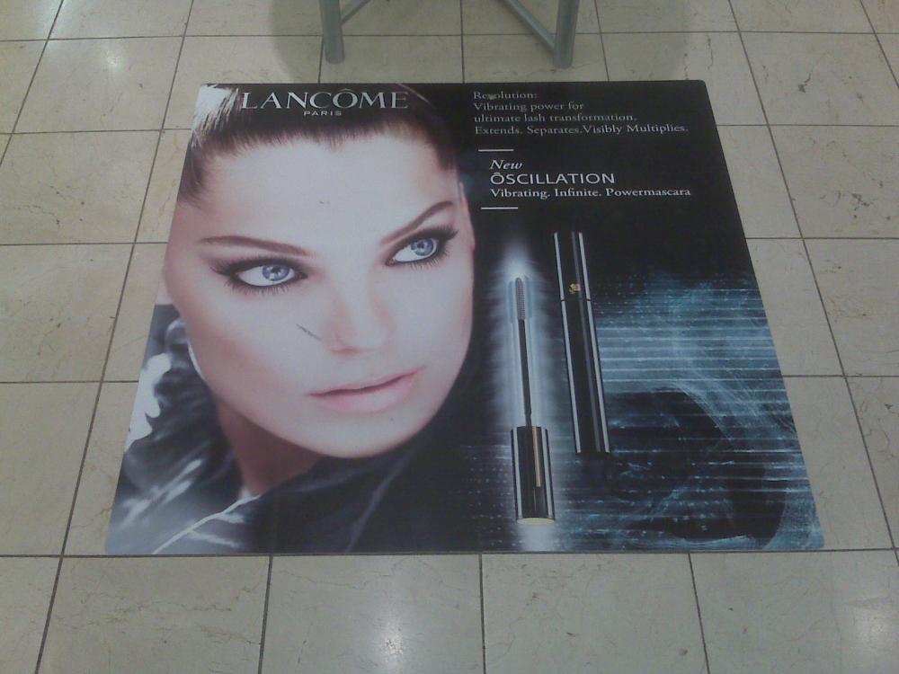 Floor graphic advertisement for Lancôme featuring a model's close-up with product promotion for Oscillation mascara.