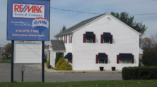 Monument sign for RE/MAX Town & Country displayed in front of a white building with black awnings.