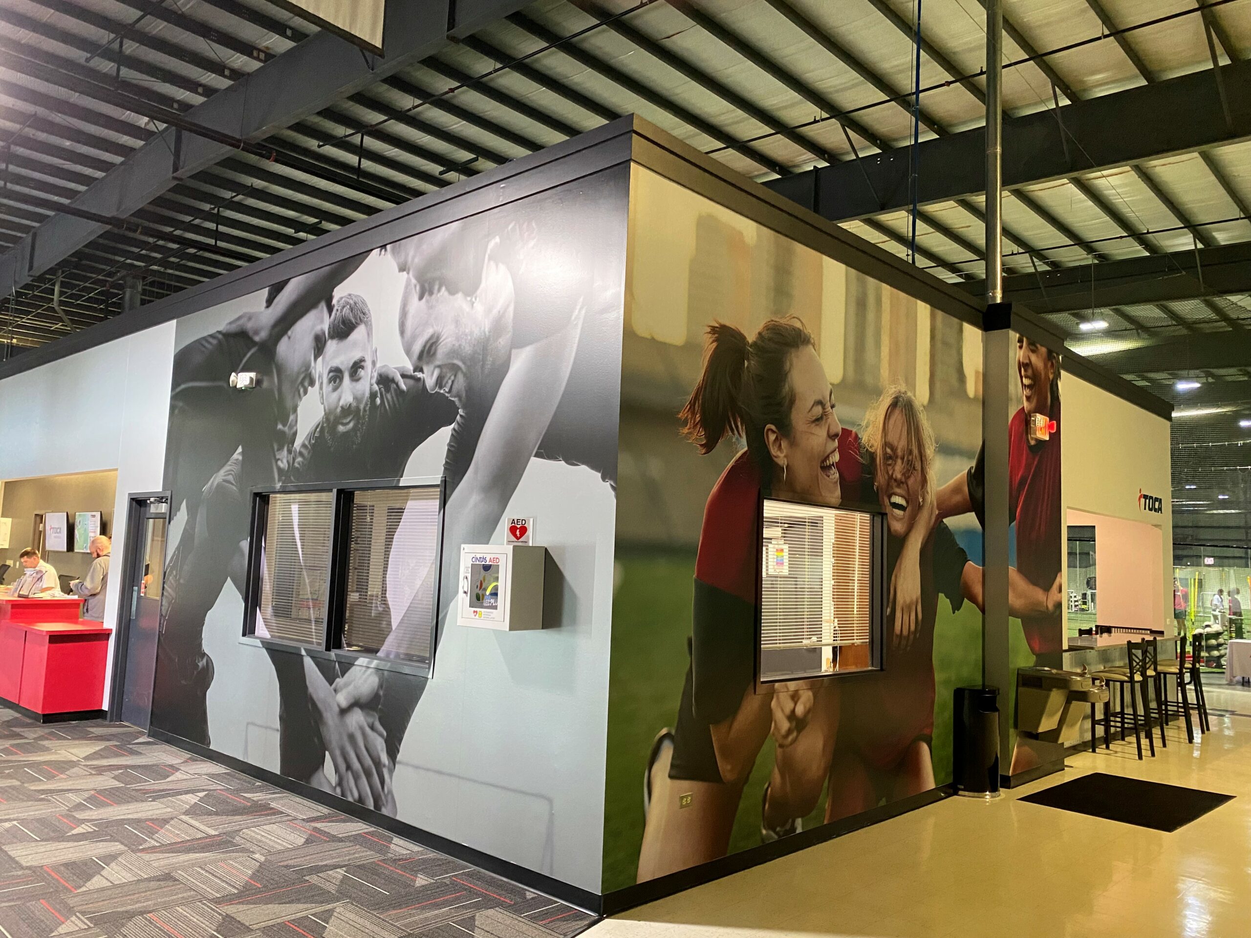 Wall mural featuring dynamic black-and-white and color images of athletes celebrating, installed in a sports facility lobby.
