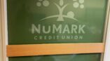 Frosted vinyl graphics featuring Numark Credit Union logo on green glass panel with wood accent.