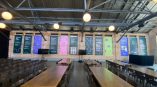 Large environmental graphics installation on brick wall in event space, featuring colorful informational panels and seating area.