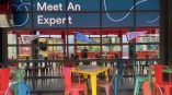 Glass partition with 'Meet An Expert' wall graphic and hanging banner signs for 'Intelligence,' 'Class Studio,' and 'Integration.'