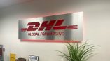 Dimensional acrylic sign featuring the DHL logo and 'GLOBAL FORWARDING' text with illuminated edges in an office lobby.