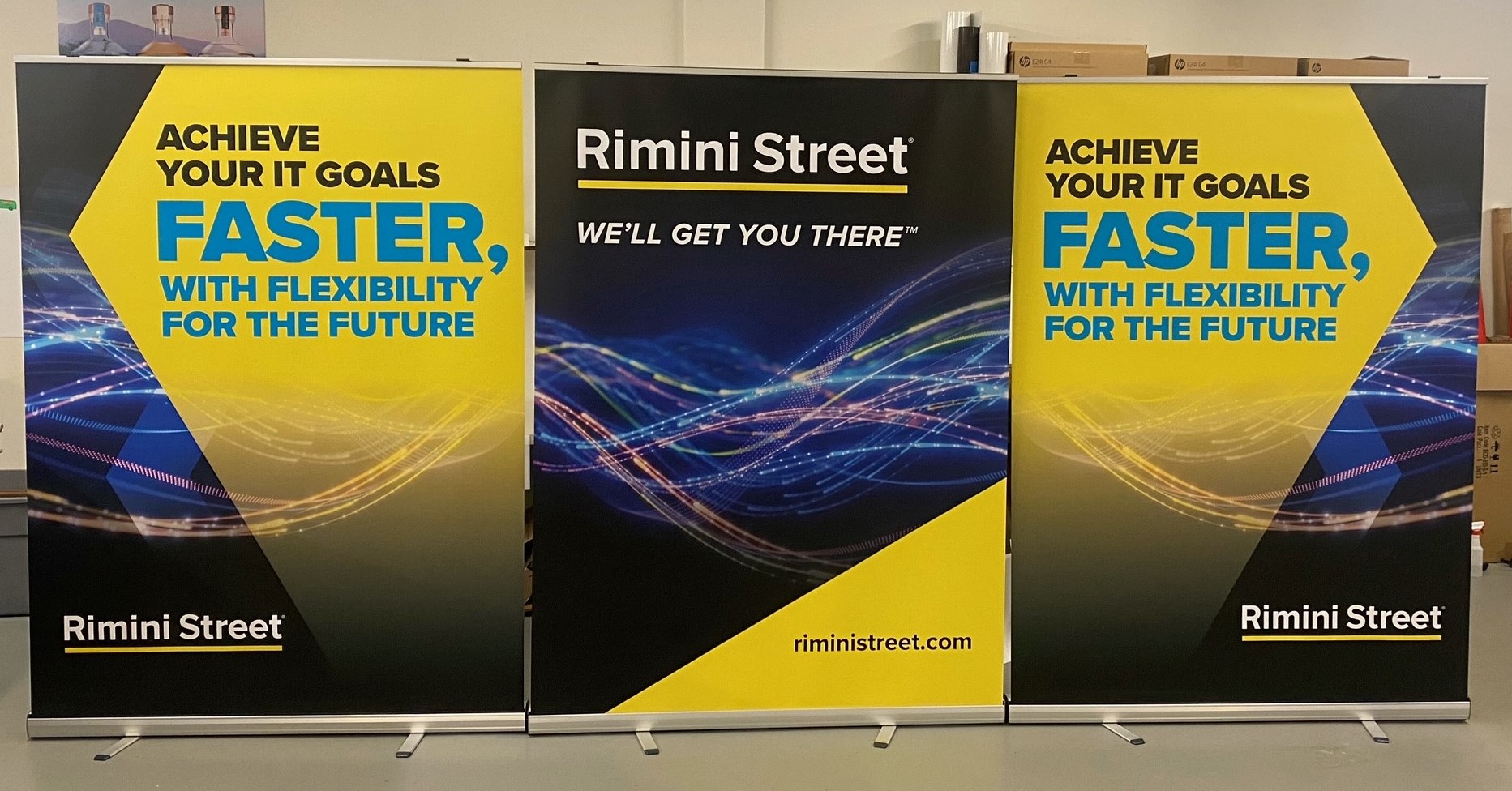 Retractable banners for Rimini Street featuring a yellow and blue design with IT goals messaging.