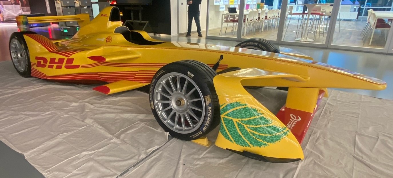 DHL-branded race car displayed on a white mat, featuring yellow and red graphics and leaf design on the side.