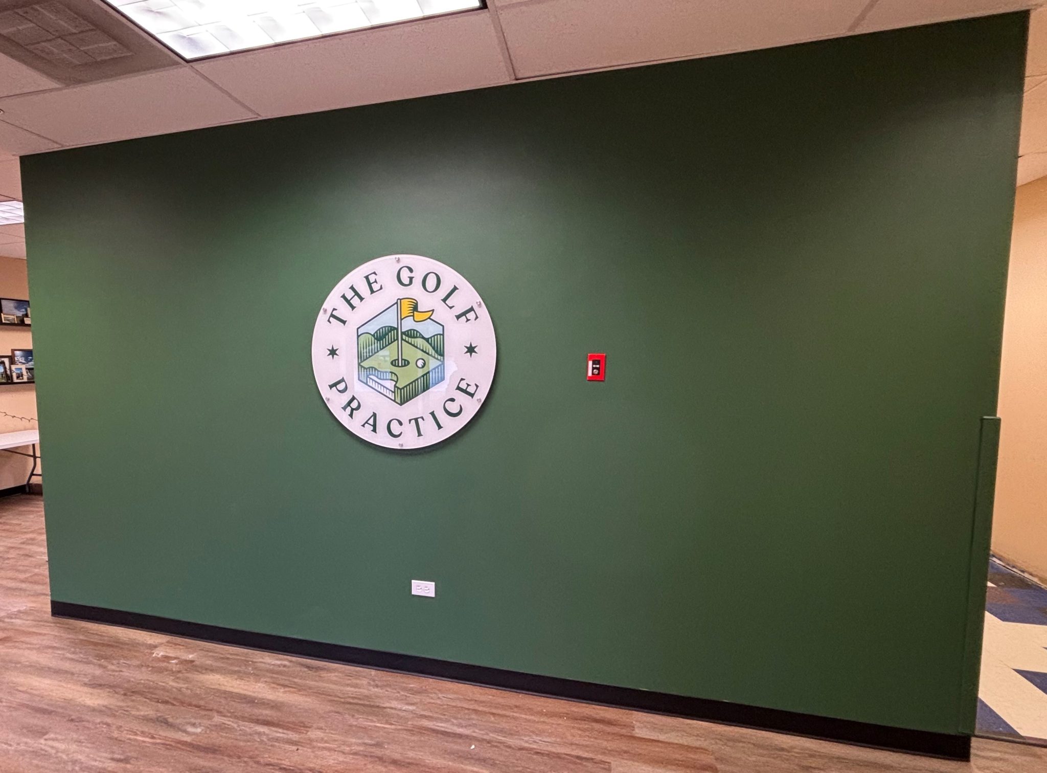 Dimensional wall sign for The Golf Practice featuring a circular logo on a green-painted wall.