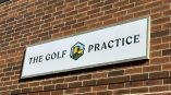 Acrylic exterior sign for The Golf Practice featuring green and gold graphic elements on a brick wall.