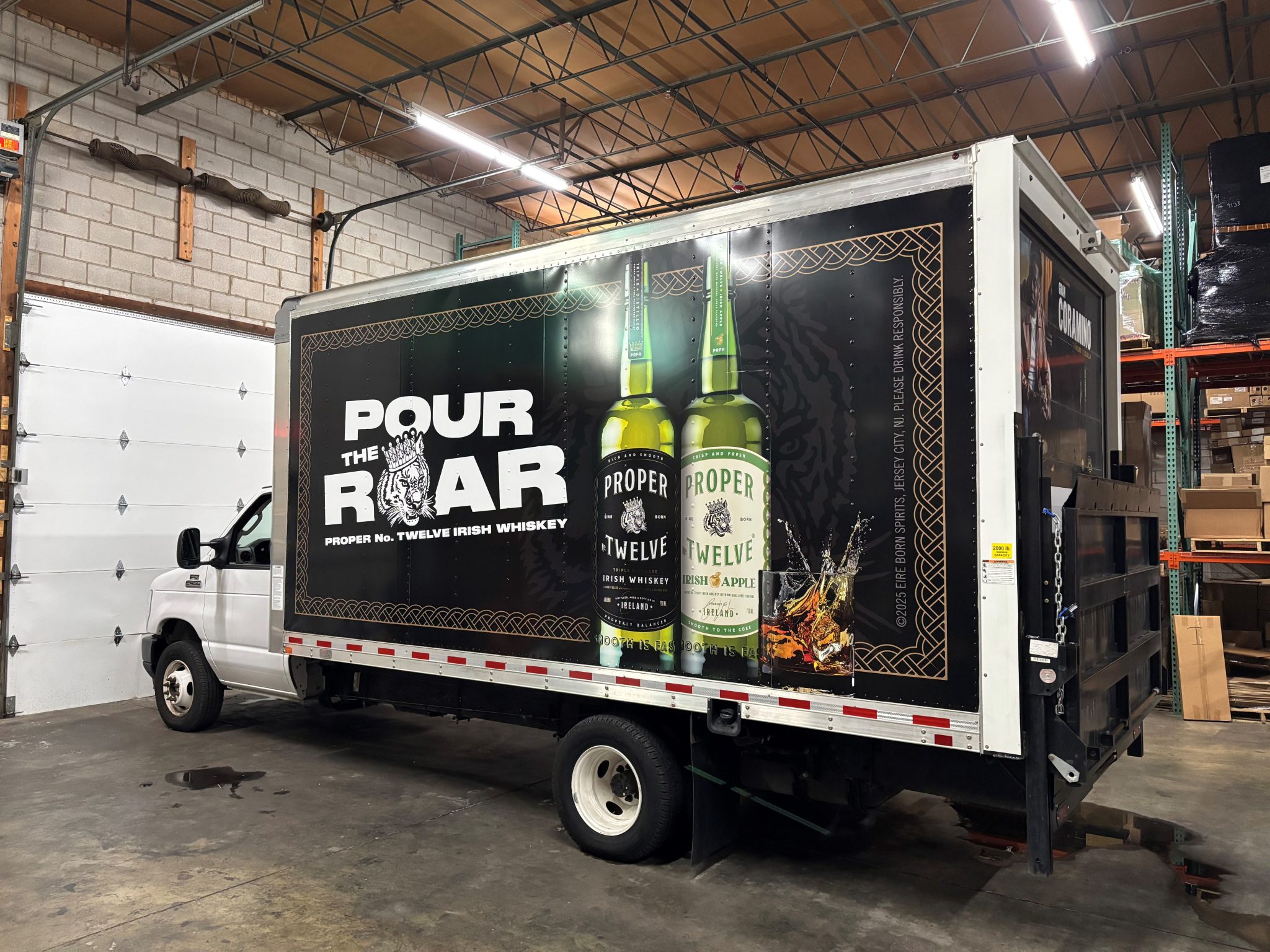 Full truck wrap for Proper No. Twelve Irish Whiskey featuring bold graphics and vibrant imagery inside a warehouse environment.