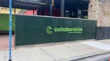 Dimensional lettering sign for 'collaborative' in bright green on a dark green wall in an urban setting.