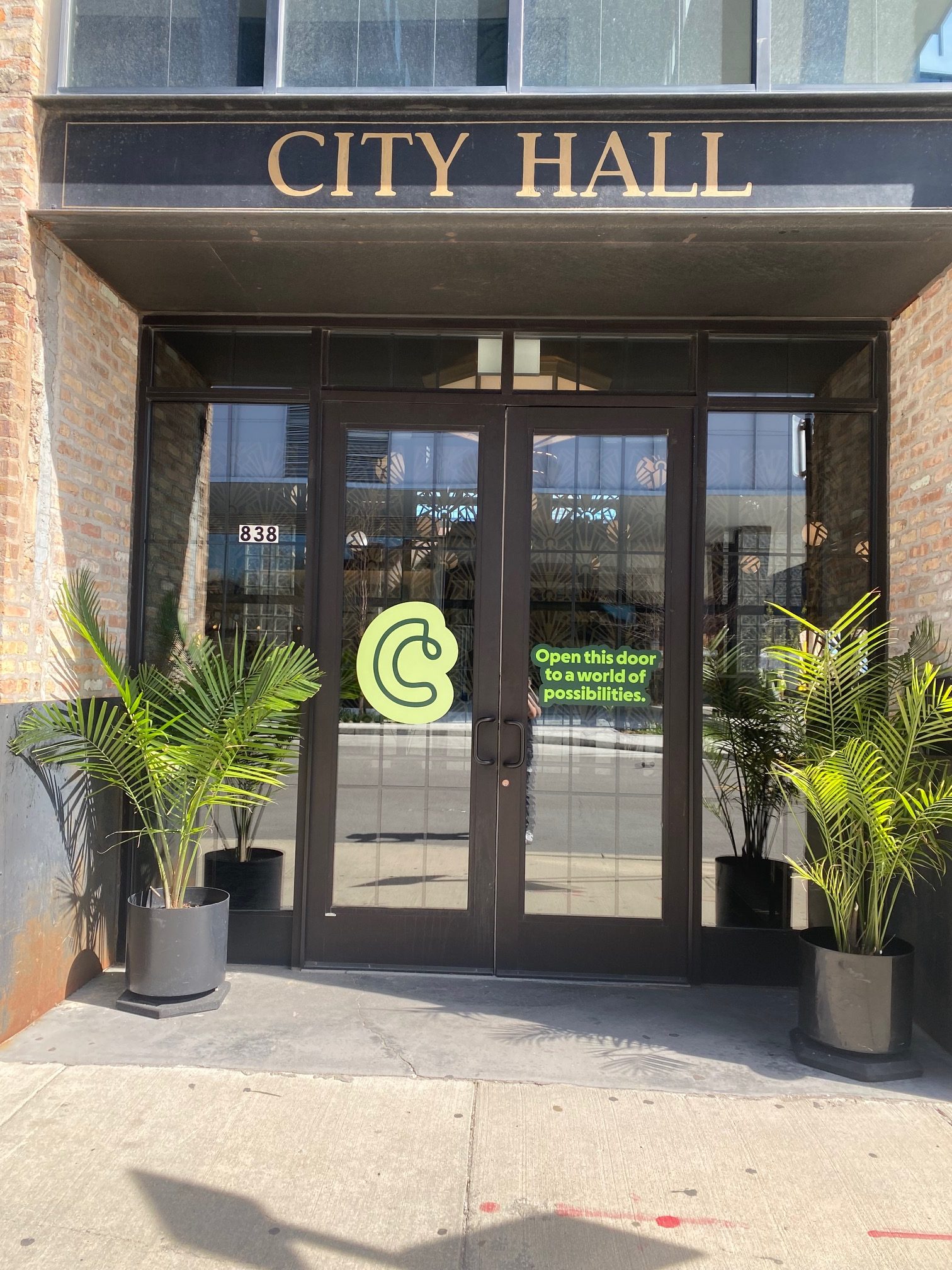 Entrance to City Hall featuring dimensional lettering, decorative planter pots, and window graphics with a motivational message.