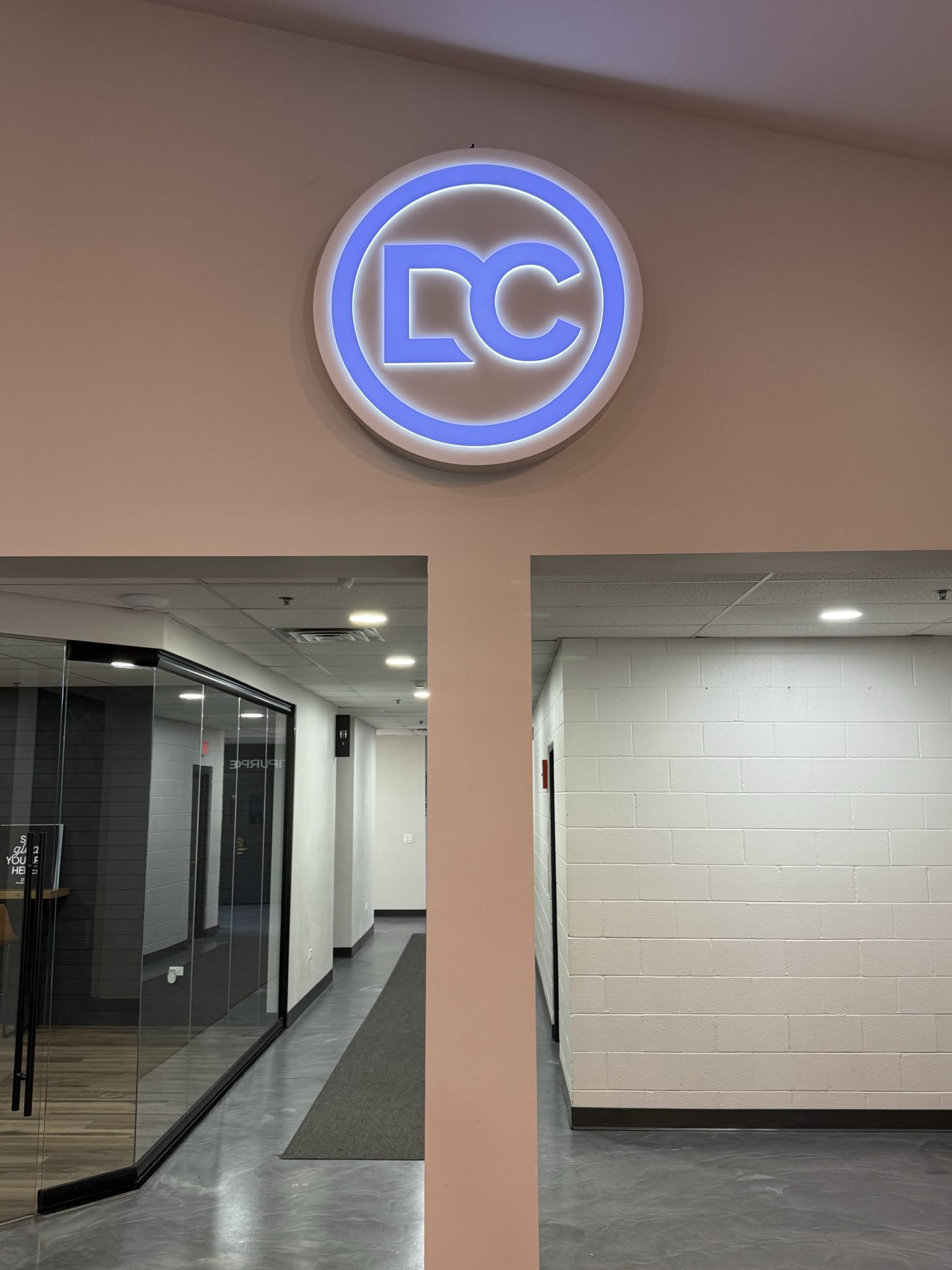 Illuminated channel letter sign featuring 'DC' in blue on a white wall above an entryway, displayed in a contemporary interior.
