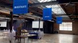 Hanging environmental graphics featuring blue panels with the words 'INVESTIGATE,' 'EXPOSE,' and 'CHANGE' in a large event space.