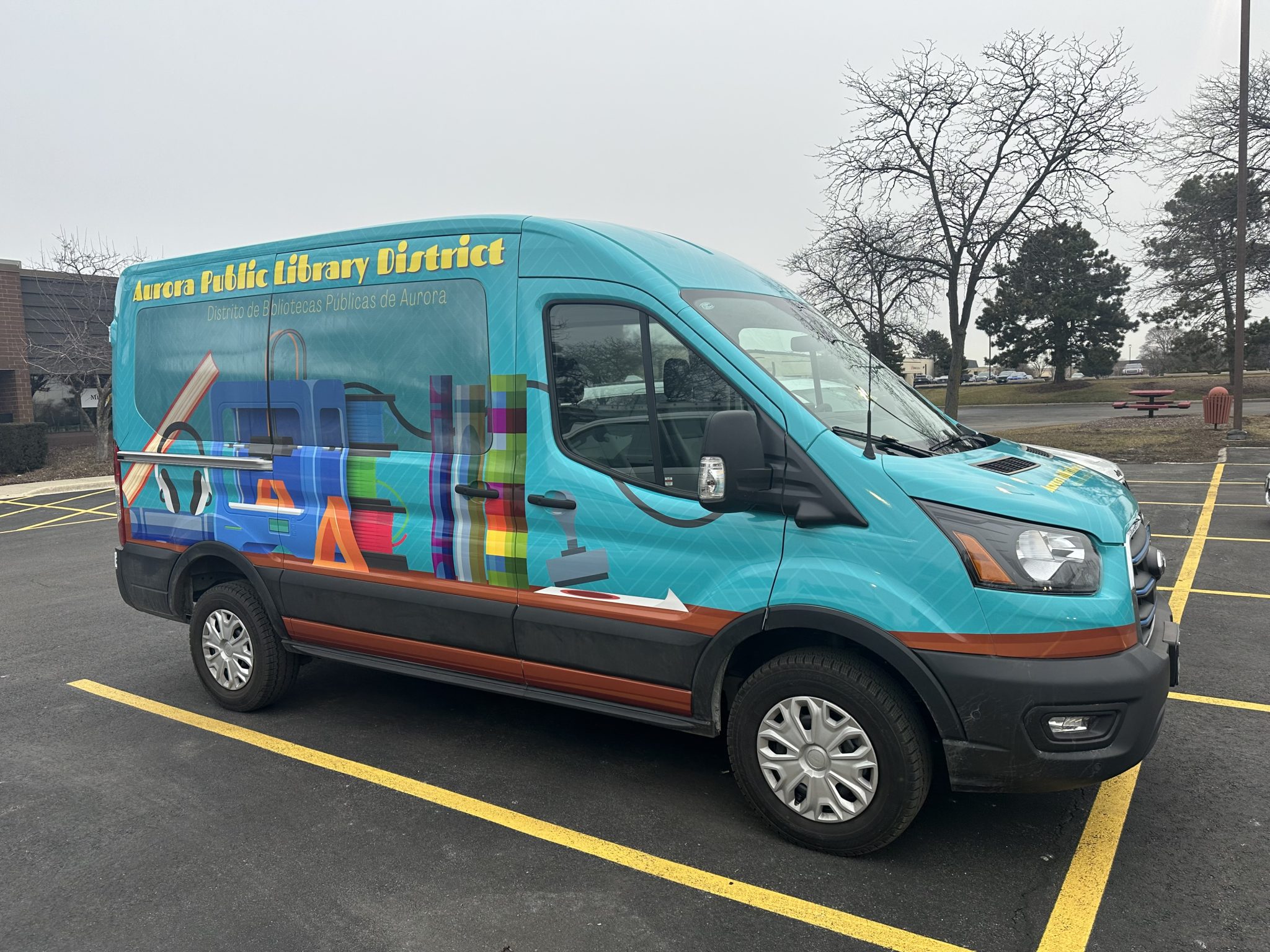 Full van wrap for Aurora Public Library District featuring colorful graphics and icons of library tools.