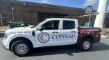 Full vehicle wrap for Conrad Roofing with white and maroon graphics, contact information, and logo displayed prominently.