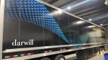 Full trailer wrap for Darwill featuring a black background with blue dot patterns and the slogan “Marketing That Drives Results.”