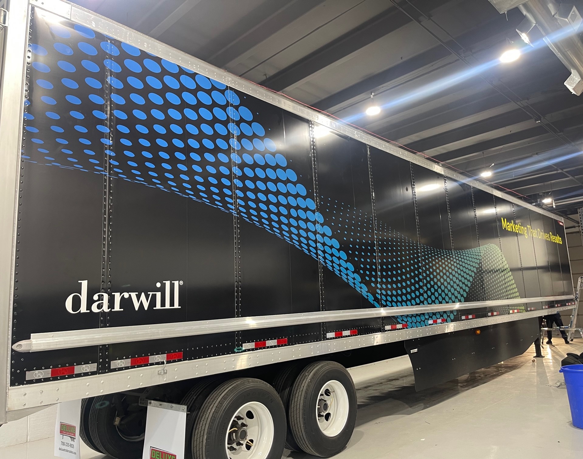 Full trailer wrap for Darwill featuring a black background with blue dot patterns and the slogan “Marketing That Drives Results.”