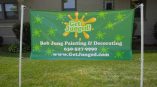 Outdoor banner for Bob Jung Painting & Decorating, featuring green background with paint splash graphics and contact information.