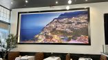 large wall mural of coastal village scene displayed in restaurant, featuring beach and hillside buildings