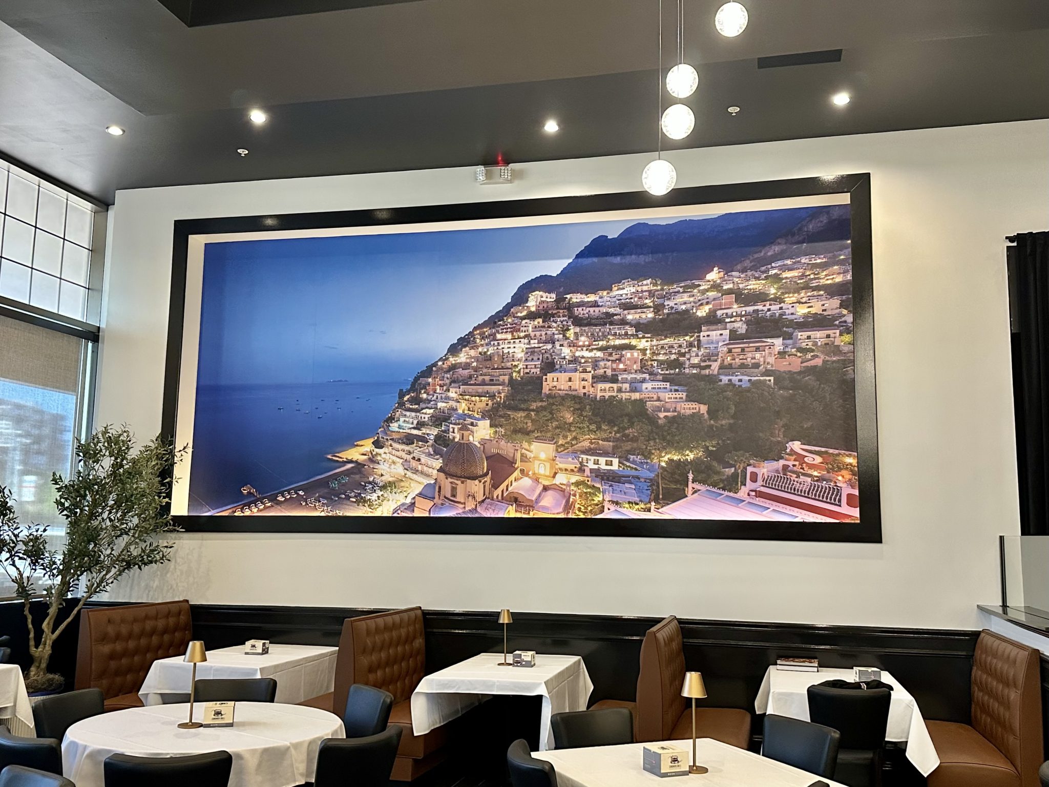large wall mural of coastal village scene displayed in restaurant, featuring beach and hillside buildings