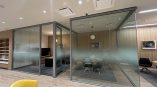 Frosted vinyl graphics applied to glass conference room walls, featuring modern seating and wood paneling in an office setting.
