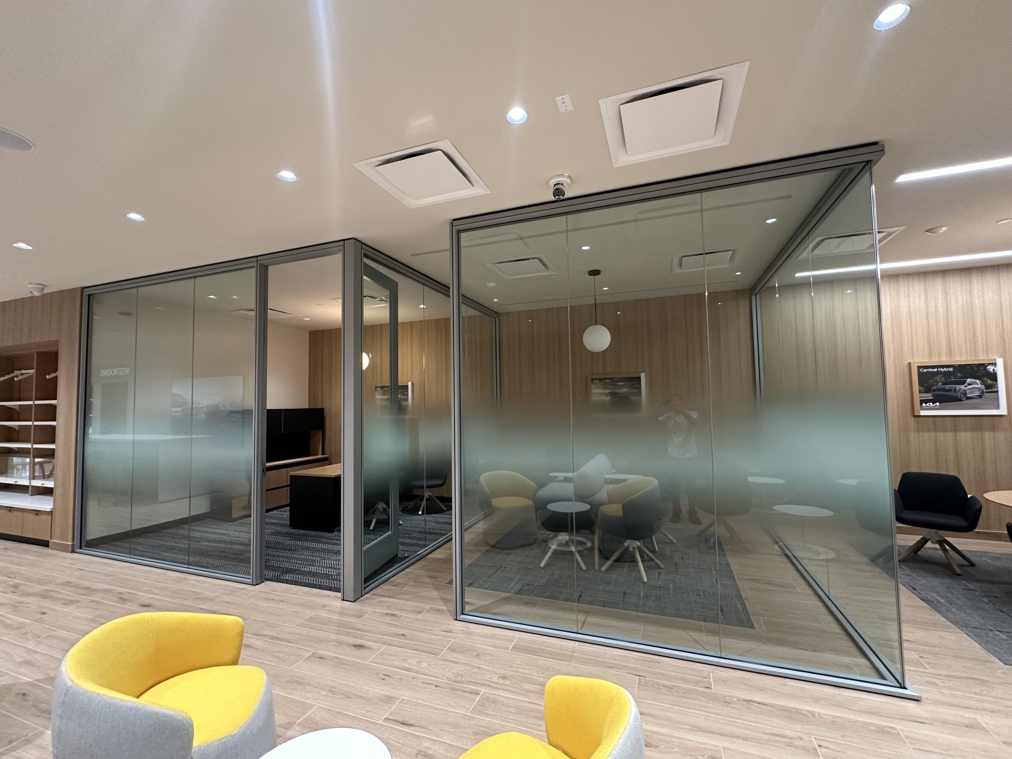 Frosted vinyl graphics applied to glass conference room walls, featuring modern seating and wood paneling in an office setting.