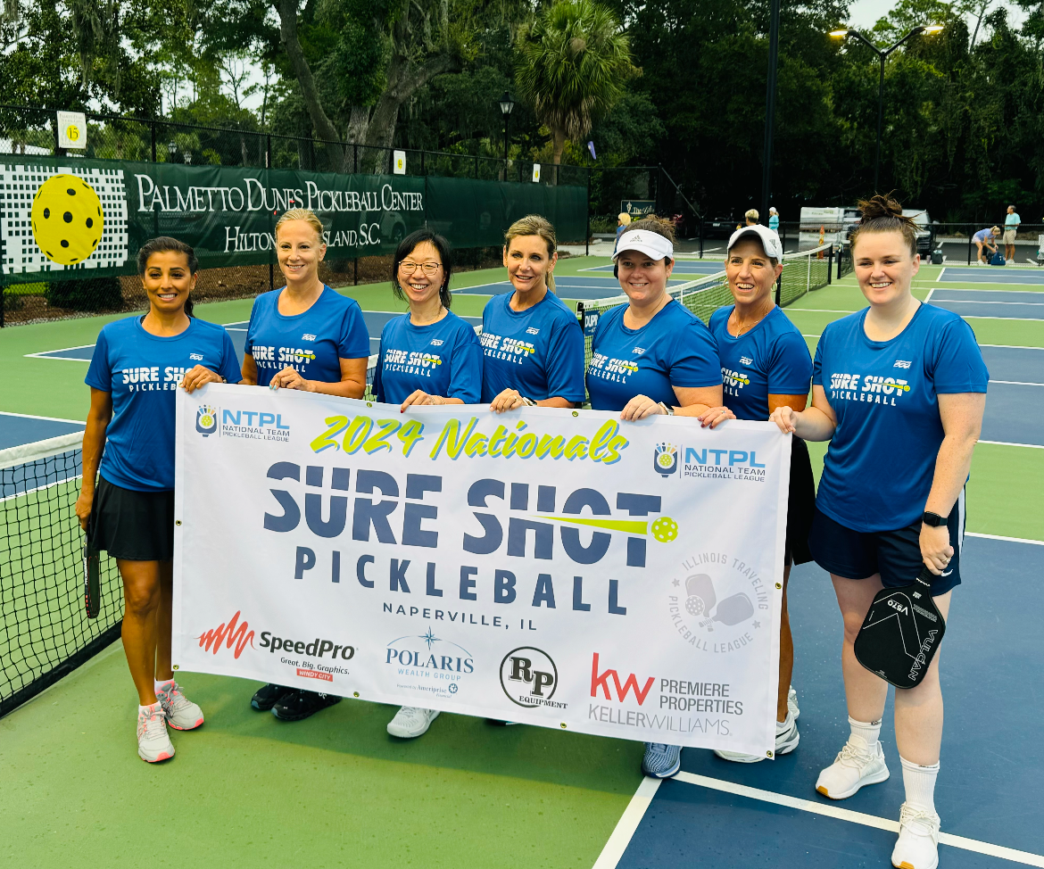 Team of female pickleball players in blue shirts holding a banner for 'Sure Shot Pickleball' at a tournament in Hilton Head, SC.