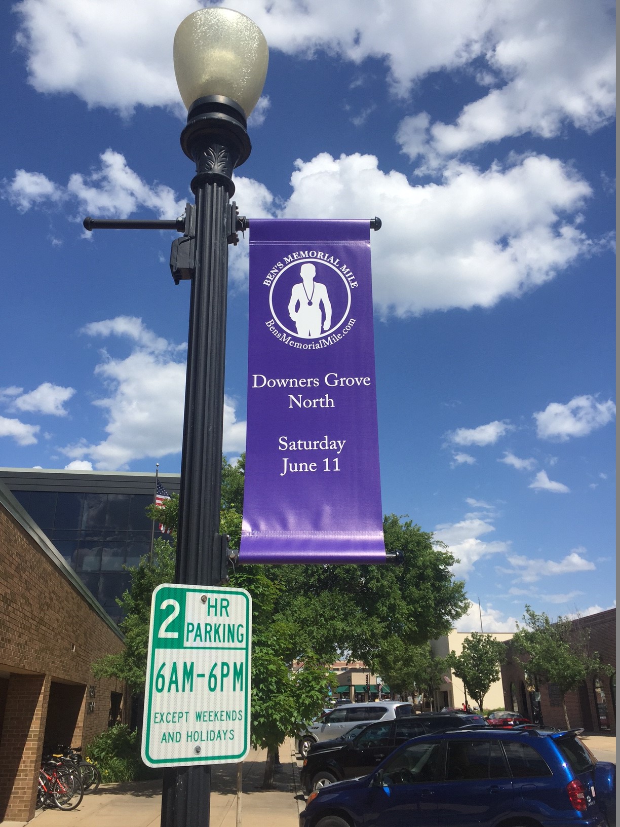 Purple street banner for Ben's Memorial Mile in Downers Grove, featuring event details and a runner graphic.